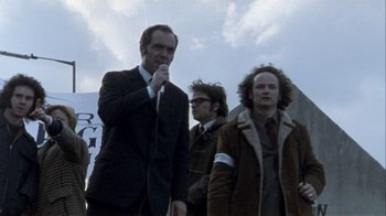 Movie still from “Bloody Sunday” (2002), directed by Paul Greengrass – A man in a suit speaking to a group of people; Medium shot, Low angle