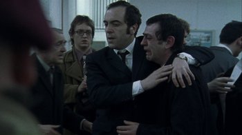 Movie still from “Bloody Sunday” (2002), directed by Paul Greengrass – A group of men standing around each other in a room; Medium shot, Over the shoulder angle
