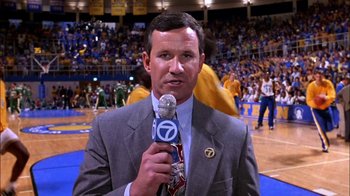 Movie still from “Blue Chips” (1994), directed by William Friedkin – A man in a suit and tie holding a microphone; Close Up shot, Low angle