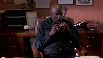 Movie still from “Blue Chips” (1994), directed by William Friedkin – A man sitting in a chair and playing a flute; Medium shot, Low angle
