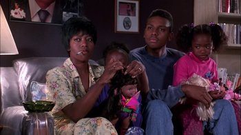 Movie still from “Blue Chips” (1994), directed by William Friedkin – A family sitting on a couch and smoking a cigarette; Medium shot, High angle