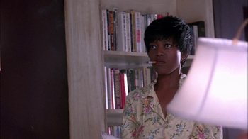 Movie still from “Blue Chips” (1994), directed by William Friedkin – A woman is smoking a cigarette in front of a book shelf; Close Up shot, Low angle