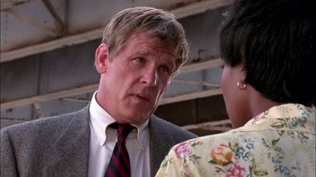 Movie still from “Blue Chips” (1994), directed by William Friedkin – A man in a suit talking to a woman in a floral dress; Close Up shot, Over the shoulder angle