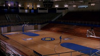 Movie still from “Blue Chips” (1994), directed by William Friedkin – A man standing on a basketball court in a gym; Extreme Wide shot, High angle
