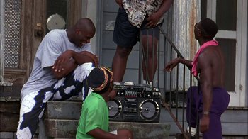 Movie still from “Blue Chips” (1994), directed by William Friedkin – A group of people sitting on a porch with a radio; Wide shot, Low angle
