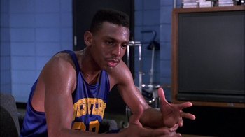 Movie still from “Blue Chips” (1994), directed by William Friedkin – A man in a blue and yellow basketball uniform sitting in front of a tv; Close Up shot, Over the shoulder angle