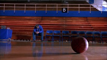 Movie still from “Blue Chips” (1994), directed by William Friedkin – A man sitting on a chair next to a basketball court; Wide shot, High angle