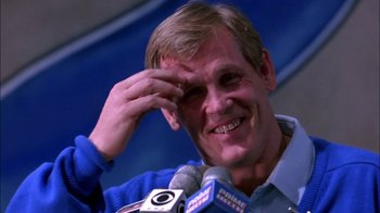Movie still from “Blue Chips” (1994), directed by William Friedkin – A man smiles while talking into a microphone at a press conference; Close Up shot, Low angle