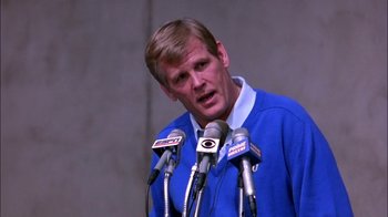 Movie still from “Blue Chips” (1994), directed by William Friedkin – A man in a blue sweater is speaking into microphones; Close Up shot, Low angle