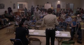 Movie still from “Blue Collar” (1978), directed by Paul Schrader – A group of people sitting in a room with tables and chairs; Wide shot, High angle
