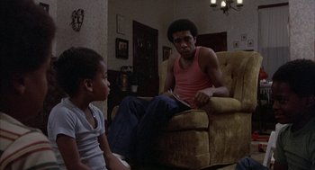 Movie still from “Blue Collar” (1978), directed by Paul Schrader – A man sitting on a chair talking to a young girl; Medium shot, Over the shoulder angle