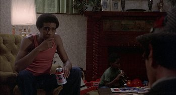 Movie still from “Blue Collar” (1978), directed by Paul Schrader – A man sitting in front of a fireplace holding a can of soda; Medium shot, Low angle