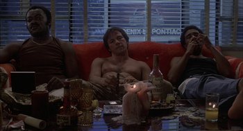 Movie still from “Blue Collar” (1978), directed by Paul Schrader – A man sitting on top of a red couch next to two other people; Wide shot, Low angle