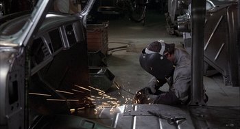 Movie still from “Blue Collar” (1978), directed by Paul Schrader – A man wearing a welding helmet is working in a garage; Medium shot, High angle