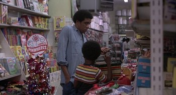 Movie still from “Blue Collar” (1978), directed by Paul Schrader – A man and a child in a store looking at items on a table; Medium shot, Over the shoulder angle