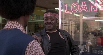 Movie still from “Blue Collar” (1978), directed by Paul Schrader – A man wearing a head band standing in front of a store; Medium shot, Over the shoulder angle