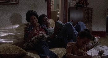 Movie still from “Blue Collar” (1978), directed by Paul Schrader – A woman sitting on a couch reading a book while a man sits on a couch next to her; Medium shot, High angle