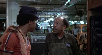 Movie still from “Blue Collar” (1978), directed by Paul Schrader – Two men are talking to each other in an industrial setting; Medium shot, Over the shoulder angle