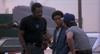 Movie still from “Blue Collar” (1978), directed by Paul Schrader – A group of men standing next to each other talking; Medium shot, Over the shoulder angle