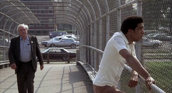 Movie still from “Blue Collar” (1978), directed by Paul Schrader – A man is playing tennis on a tennis court; Wide shot, Over the shoulder angle