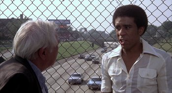 Movie still from “Blue Collar” (1978), directed by Paul Schrader – A man and a woman are standing in front of a chain link fence; Medium shot, Over the shoulder angle