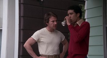 Movie still from “Blue Collar” (1978), directed by Paul Schrader – Two men standing next to each other and one of them is drinking from a cup; Medium shot, Low angle