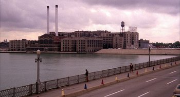 Movie still from “Blue Collar” (1978), directed by Paul Schrader – A man riding a bike down the side of a river; Extreme Wide shot, High angle