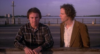 Movie still from “Blue Collar” (1978), directed by Paul Schrader – Two men sitting at a table near a body of water; Medium shot, Over the shoulder angle