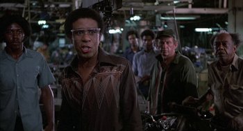 Movie still from “Blue Collar” (1978), directed by Paul Schrader – A group of men standing in a factory; Medium shot, Over the shoulder angle