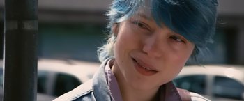 Movie still from “Blue Is the Warmest Colour” (2013), directed by Abdellatif Kechiche – A person with blue hair smiling; Close Up shot, Over the shoulder angle