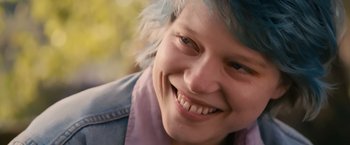 Movie still from “Blue Is the Warmest Colour” (2013), directed by Abdellatif Kechiche – A person with blue hair smiling; Close Up shot, Low angle