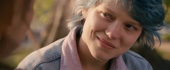 Movie still from “Blue Is the Warmest Colour” (2013), directed by Abdellatif Kechiche – A person with blue hair smiling; Close Up shot, Over the shoulder angle