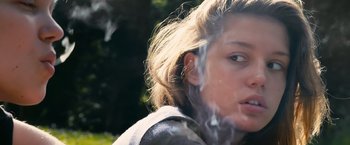 Movie still from “Blue Is the Warmest Colour” (2013), directed by Abdellatif Kechiche – A young woman smoking a cigarette outside in the sun; Close Up shot, Low angle