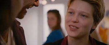 Movie still from “Blue Is the Warmest Colour” (2013), directed by Abdellatif Kechiche – A person smiling with another person in the background; Close Up shot, Over the shoulder angle