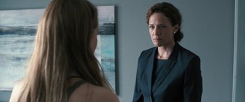 A woman in a suit looking in the mirror while talking to another woman