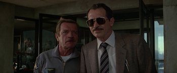 Movie still from “Blue Thunder” (1983), directed by John Badham – A man and a man in a suit and sunglasses; Close Up shot, Low angle