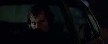 Movie still from “Blue Thunder” (1983), directed by John Badham – A man sitting in the back seat of a car; Close Up shot, Over the shoulder angle