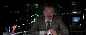 Movie still from “Blue Thunder” (1983), directed by John Badham – A man sitting at a table in front of a city skyline at night; Close Up shot, Low angle