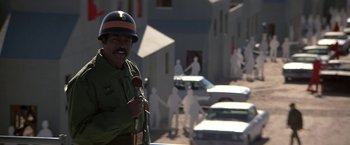 Movie still from “Blue Thunder” (1983), directed by John Badham – A man in a police uniform holding a microphone; Medium shot, Over the shoulder angle