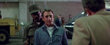 Movie still from “Blue Thunder” (1983), directed by John Badham – A man standing next to another man in a military uniform; Medium shot, Over the shoulder angle