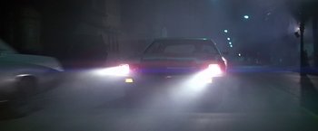 Movie still from “Blue Thunder” (1983), directed by John Badham – The headlights of a car on the street at night; Wide shot, Low angle