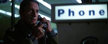 Movie still from “Blue Thunder” (1983), directed by John Badham – A man holding a phone up to his ear while standing in front of a sign; Close Up shot, Low angle