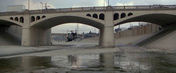 Movie still from “Blue Thunder” (1983), directed by John Badham – A helicopter is flying over a river under a bridge; Extreme Wide shot, High angle