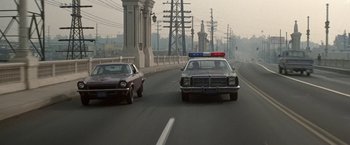Movie still from “Blue Thunder” (1983), directed by John Badham – A police car driving down a street next to another car; Wide shot, Low angle