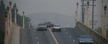 Movie still from “Blue Thunder” (1983), directed by John Badham – A couple of cars driving down a street; Extreme Wide shot, Low angle