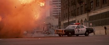 Movie still from “Blue Thunder” (1983), directed by John Badham – An explosion in a city with a police car on the side of the road; Wide shot, Low angle