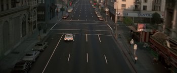 Movie still from “Blue Thunder” (1983), directed by John Badham – A white car driving down a street next to a traffic light; Extreme Wide shot, High angle