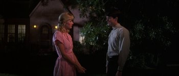 Movie still from “Blue Velvet” (1986), directed by David Lynch – A man and a woman standing next to each other in front of a tree; Medium shot, Over the shoulder angle
