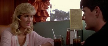 Movie still from “Blue Velvet” (1986), directed by David Lynch – A woman sitting in front of a table with a drink; Close Up shot, Over the shoulder angle