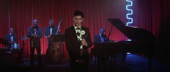 Movie still from “Blue Velvet” (1986), directed by David Lynch – A man holding a microphone in front of a band; Medium shot, Low angle